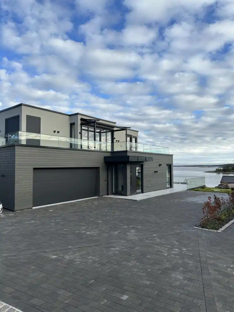 Stort, moderne hus ved vannet med glassrekkverk og garasje
